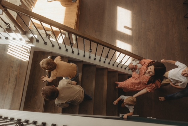 Mother carrying her newborn while walking downstairs with her children in a warm family home.