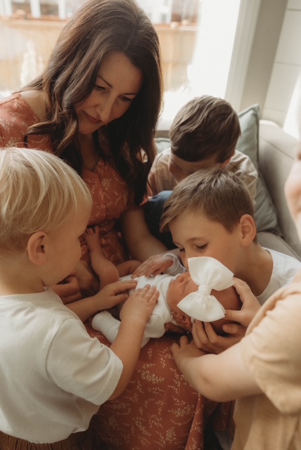 Older siblings gently meeting their newborn baby sister while mom holds her.